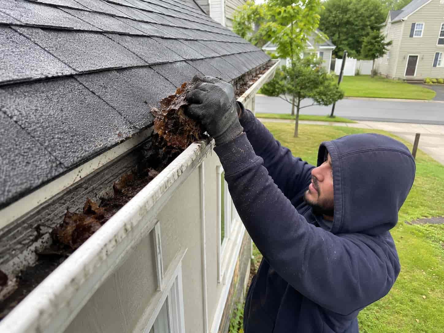 Professional technician performing gutter cleaning service on a residential home in Maryland by removing leaves and debris from seamless gutters to improve drainage and protect the roof from water damage.